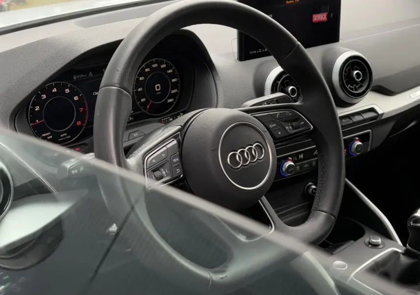 Vue intérieure de l'Audi Q2 30 TFSI S-Line 2024, volant cuir multifonction et tableau de bord digital.