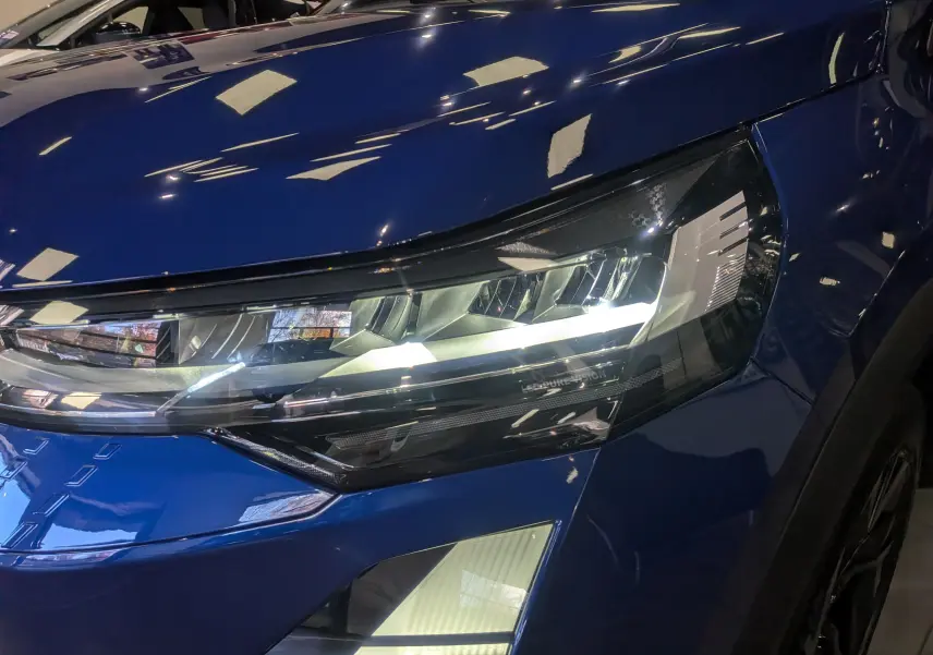 Gros plan sur le phare avant droit du Renault Captur E-TECH bleu Iron avec détails lumineux modernes et carrosserie brillante.