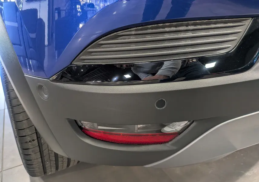 Gros plan sur le pare-chocs avant droit bleu Iron du Renault Captur E-TECH 2025 avec antibrouillard et capteurs de stationnement.