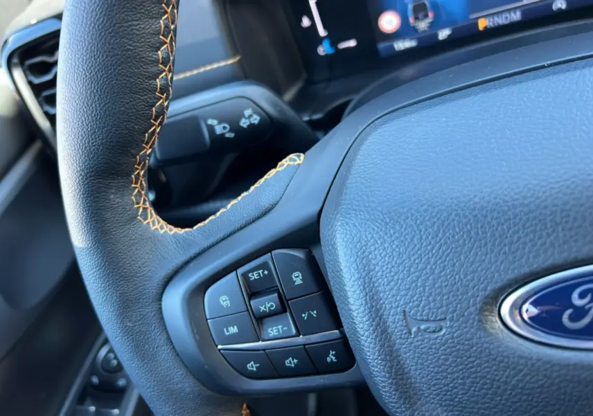 Gros plan sur le volant cuir noir avec surpiqûres marron du Ford Ranger Wildtrak Plus 2026, boutons multifonctions visibles.