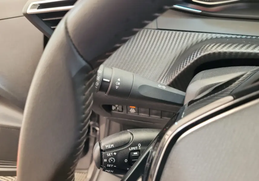 Gros plan sur le volant cuir et les commandes de régulateur de vitesse côté gauche du tableau de bord gris foncé.