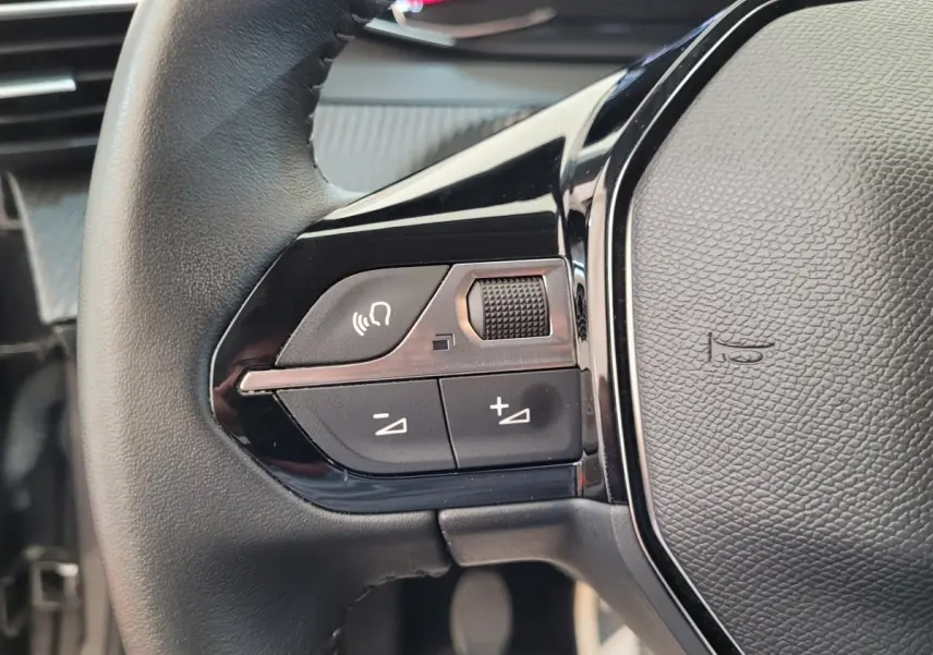 Gros plan sur la partie gauche du volant cuir de la Peugeot 208 gris foncé avec commandes vocales et volume.
