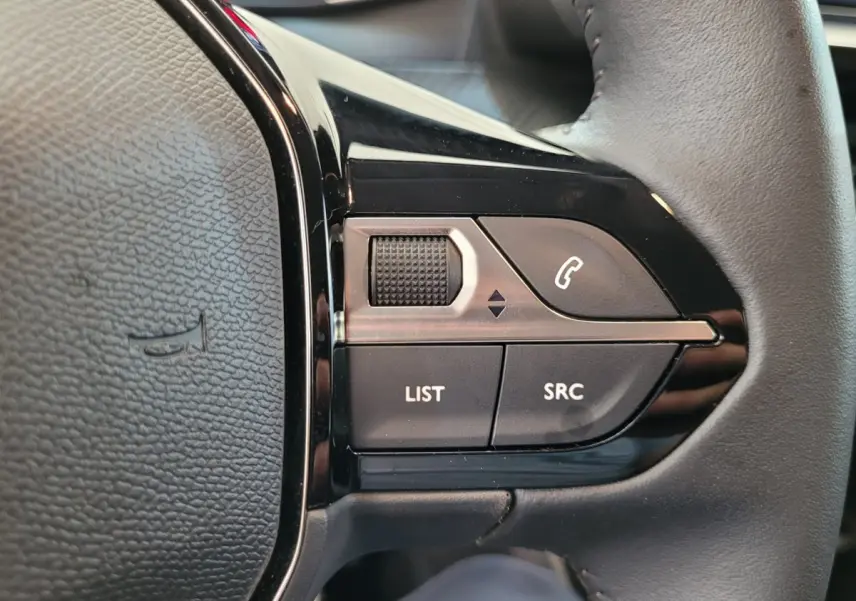 Gros plan sur les commandes gauche du volant cuir de la Peugeot 208 gris foncé 2023, avec boutons multifonctions.