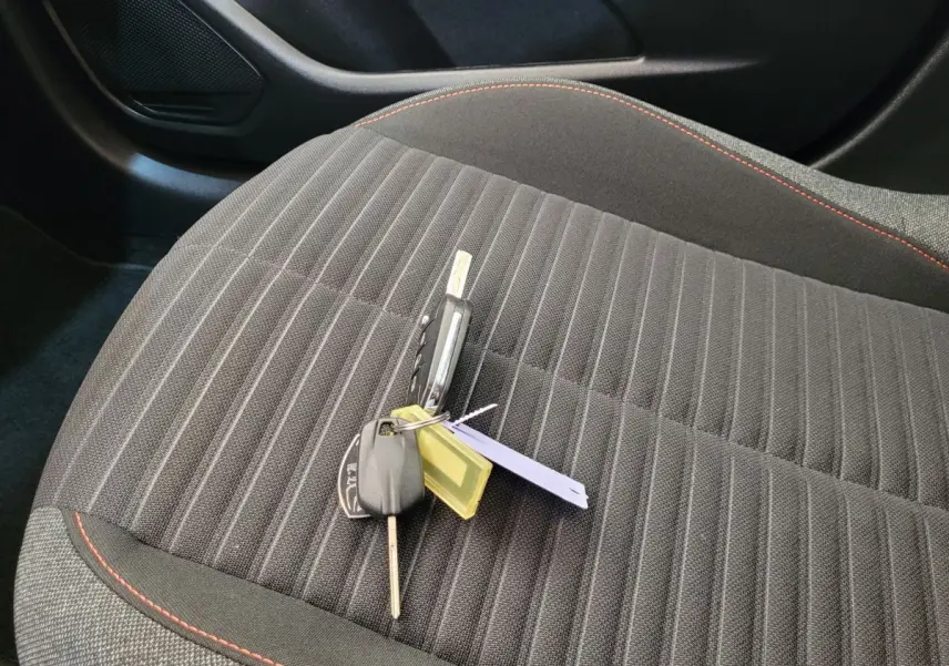 Clé de voiture posée sur le siège avant droit en tissu gris foncé avec surpiqûres rouges d'une Peugeot 208 2023.