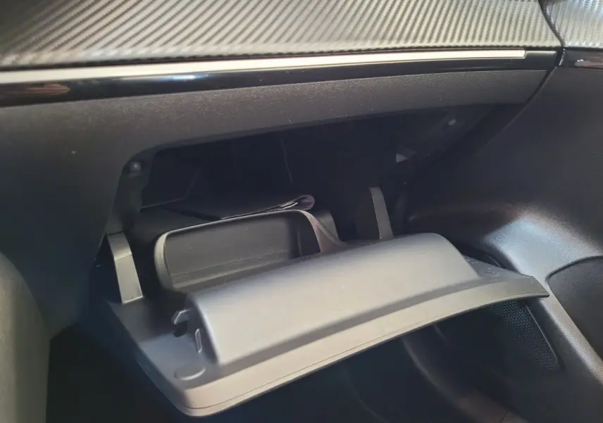 Intérieur du coffre à gants ouvert de la Peugeot 208 gris foncé, montrant le tableau de bord avec finition carbone.