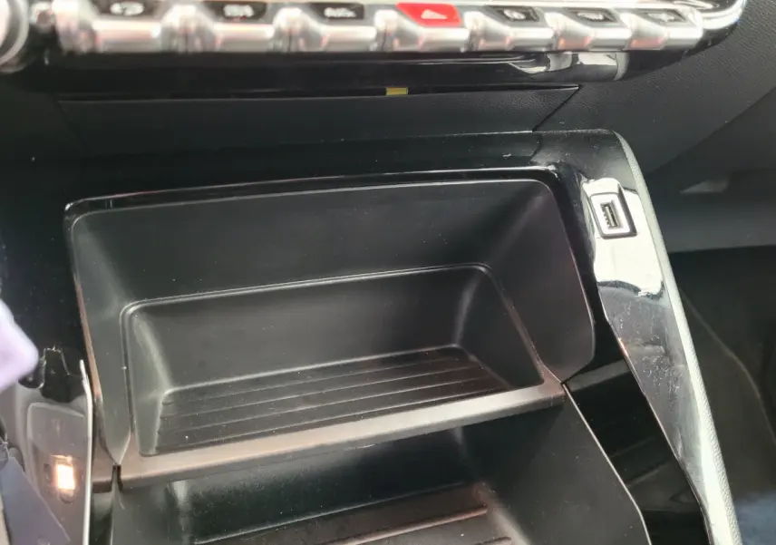 Gros plan sur le rangement central noir avec port USB du tableau de bord de la Peugeot 208 gris foncé 2023.