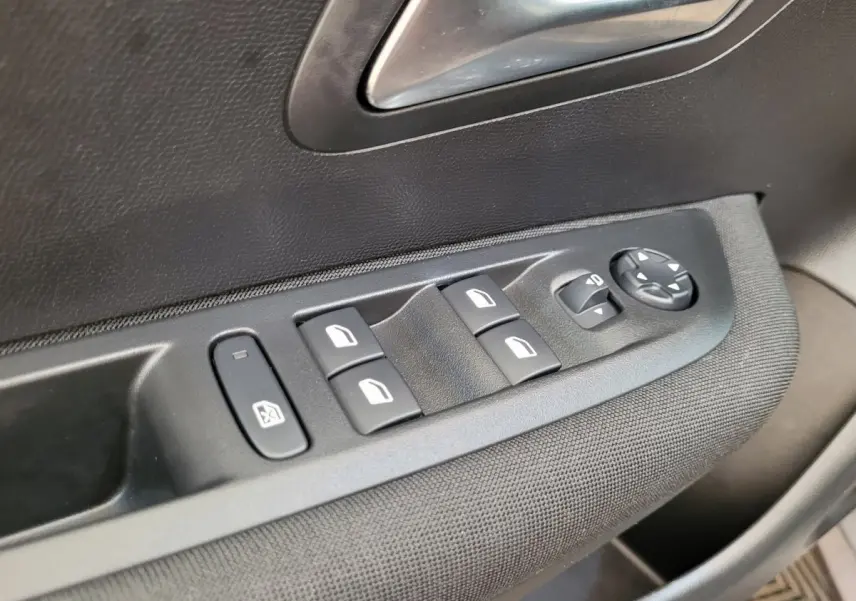 Gros plan sur les commandes de lève-vitres et réglages des rétroviseurs côté conducteur d’une Peugeot 208 gris foncé 2023.