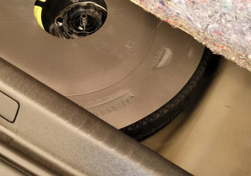 Gros plan sur la roue de secours sous la moquette du coffre d'une Peugeot 208 gris foncé 2023.