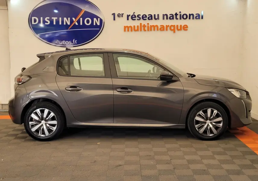 Profil côté gauche d'une Peugeot 208 BlueHDi 100 S&S Active Pack gris foncé, en intérieur avec logo Distinxion en arrière-plan.