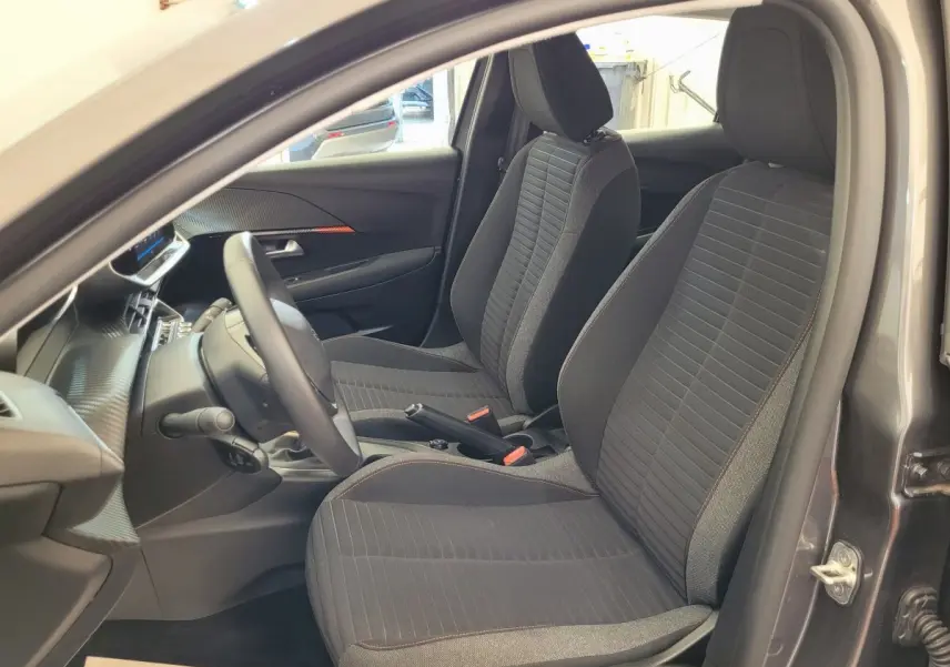 Vue intérieure côté conducteur de la Peugeot 208 BlueHDi 100 gris foncé, sièges tissu noir avec surpiqûres rouges.
