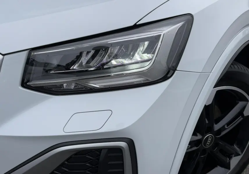 Gros plan sur le phare avant droit et la jante noire polie de l'Audi Q2 blanc glacier 30 TFSI S-Line 2024.