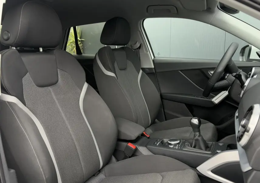 Vue intérieure côté avant droit de l’Audi Q2 30 TFSI S-Line 2024 avec sièges sport tissu gris et levier de vitesses manuel.