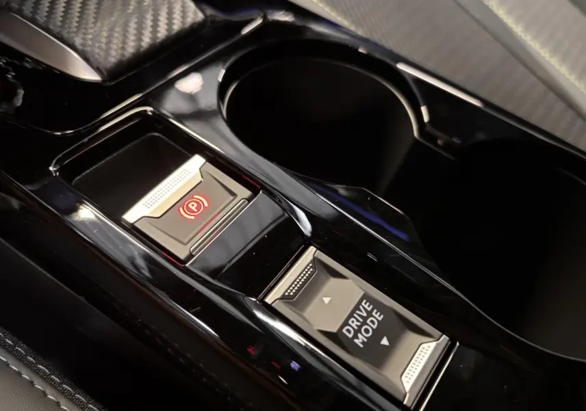 Gros plan sur la console centrale noire brillante du Peugeot 2008 gris, avec bouton frein à main électrique et sélection drive mode.