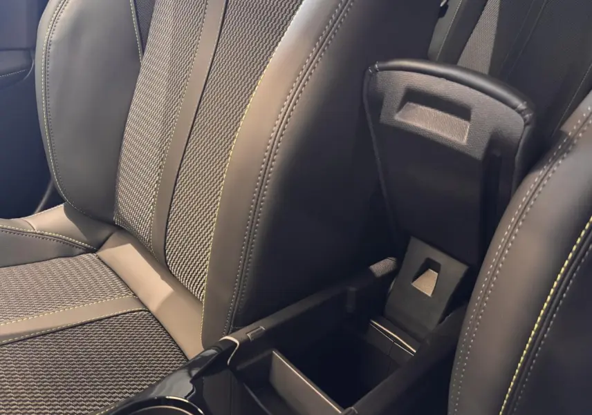 Détail de la console centrale ouverte entre les sièges avant en cuir et tissu gris du Peugeot 2008 hybride 2025.