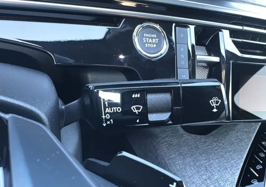 Gros plan sur la commande d’essuie-glace et bouton start du tableau de bord noir brillant d’un Peugeot 3008 New Hybrid 2025.