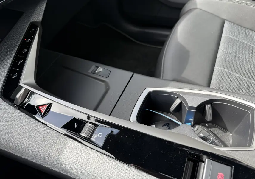 Gros plan sur la console centrale noire du Peugeot 3008 Hybrid 2026 avec porte-gobelets et commandes tactiles.