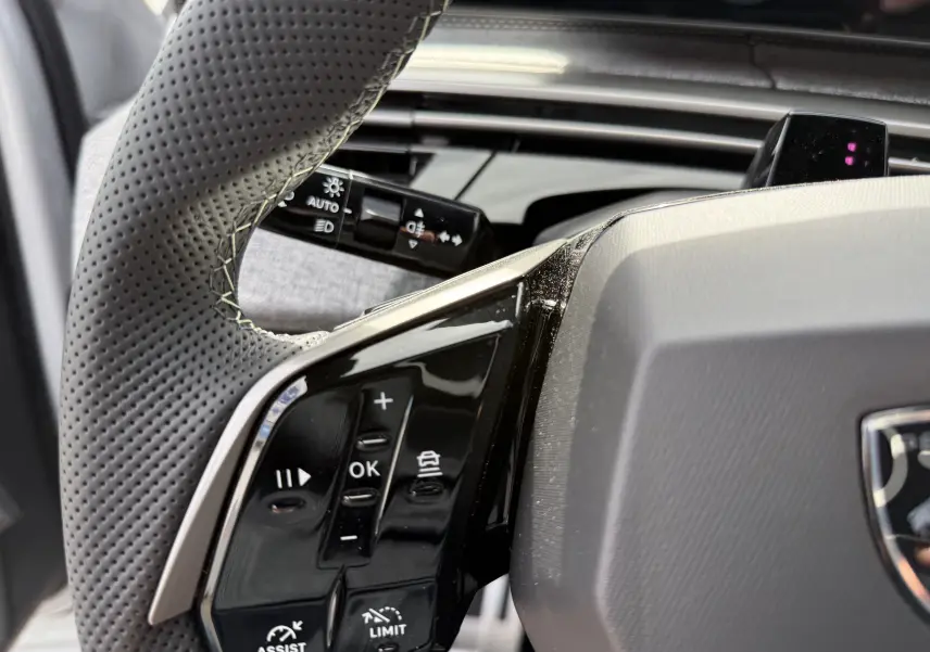 Gros plan sur le volant perforé noir et les commandes intégrées du Peugeot 3008 Hybrid 2026, intérieur moderne.