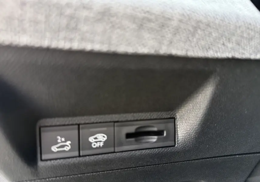 Détail intérieur des commandes noires sous tableau de bord du Peugeot 3008 Hybrid blanc, avec boutons hayon et assistance désactivée.