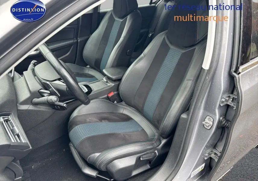 Vue intérieure côté conducteur de la Peugeot 308 gris Artense, sièges en tissu et cuir avec inserts bleus.