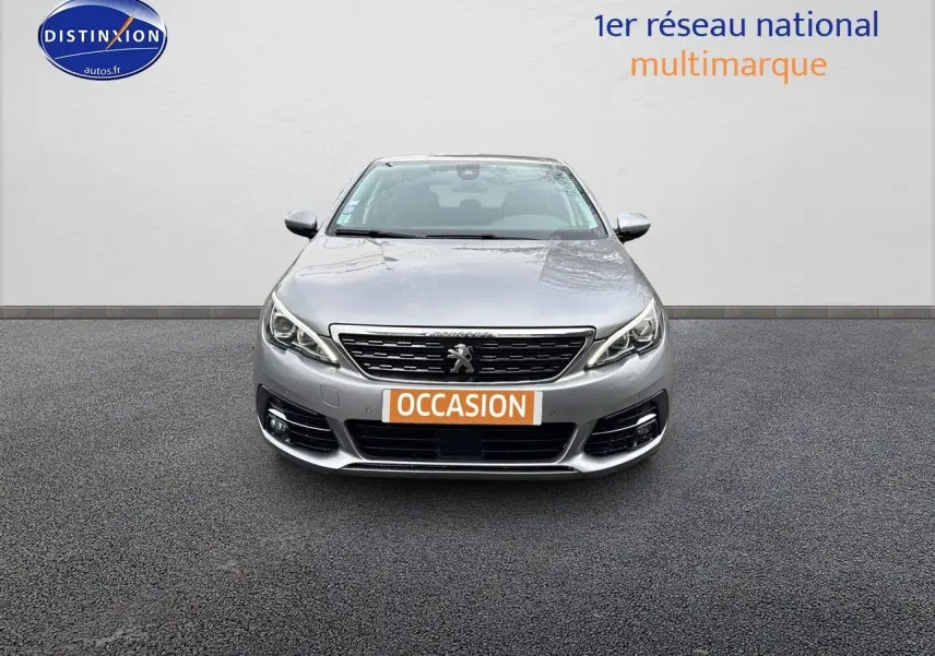 Vue frontale d'une Peugeot 308 gris Artense avec plaque "OCCASION" sur fond neutre.