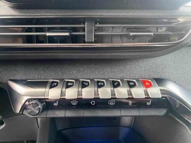 Gros plan sur la rangée de commandes chromées et noires du tableau de bord du Peugeot 3008 blanc nacré 2023.