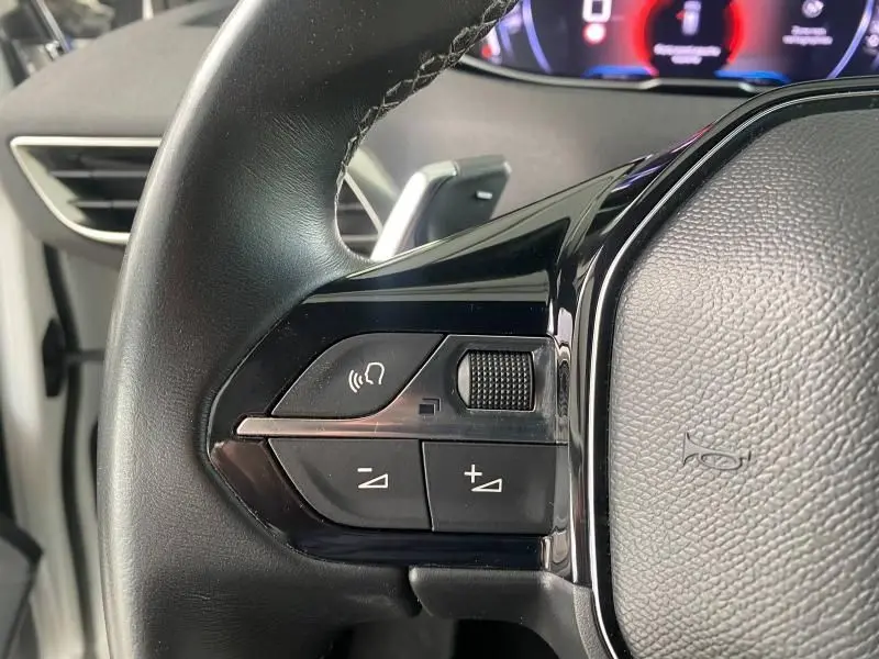 Gros plan sur les commandes audio au volant noir du Peugeot 3008 blanc nacré, avec molette et boutons de volume.