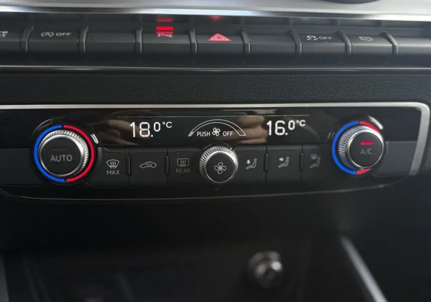 Gros plan sur la commande de climatisation automatique bi-zone du tableau de bord de l'Audi Q2 rouge Progressif 2024.