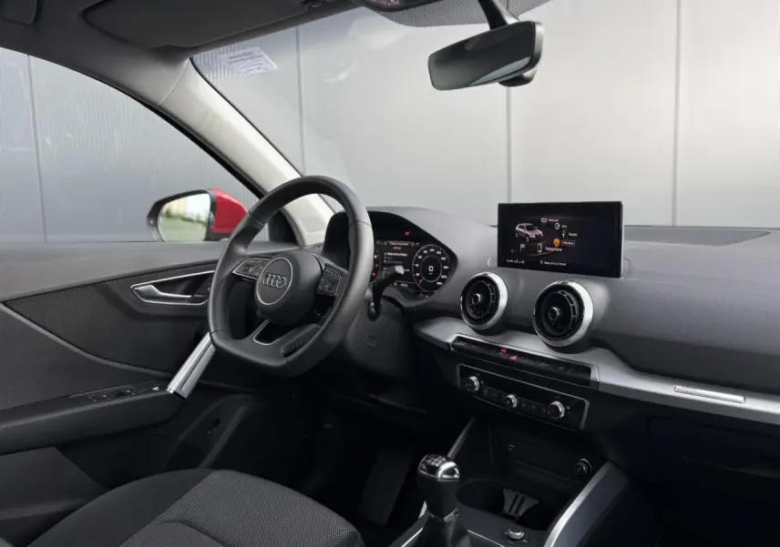 Vue intérieure côté conducteur de l'Audi Q2 30 TFSI S-Line 2024, volant cuir et écran tactile central visible.