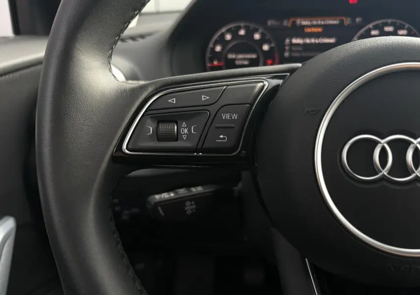 Gros plan sur le volant cuir noir de l'Audi Q2 30 TFSI S-Line 2024 avec commandes multifonctions et logo Audi central.