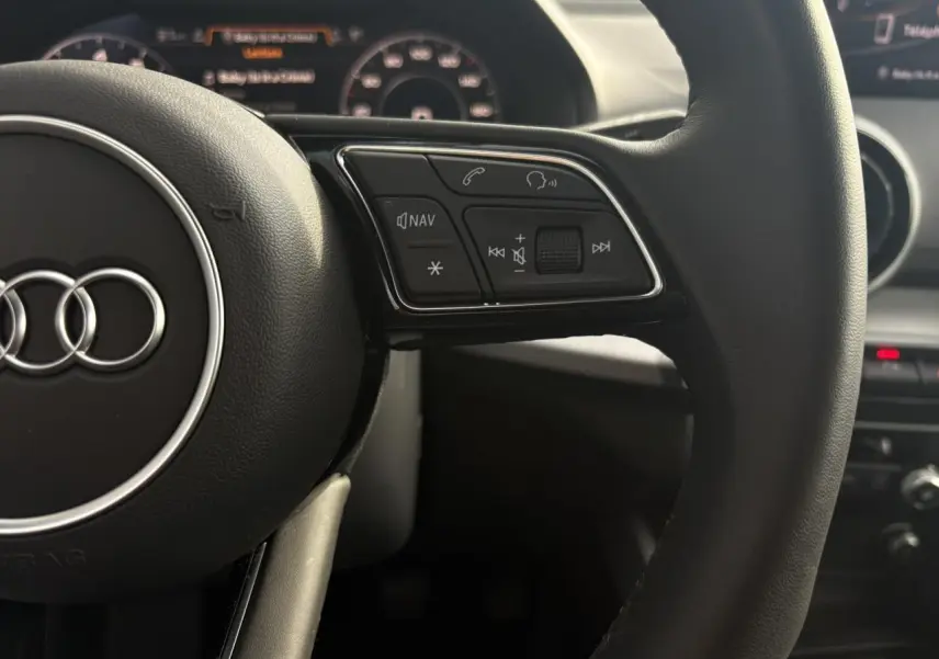 Gros plan sur le volant multifonction noir de l'Audi Q2 30 TFSI S-Line avec commandes audio et navigation visibles.