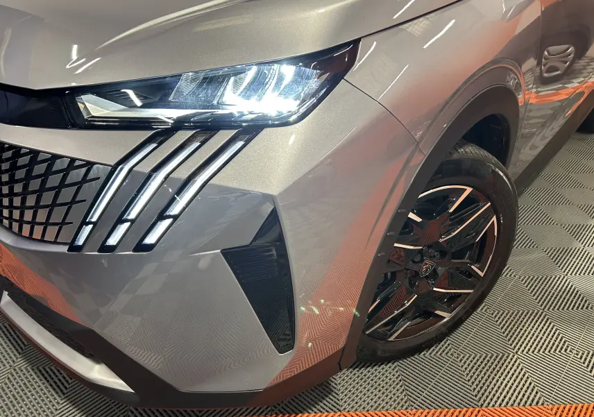 Gros plan sur l'avant droit gris Artense du Peugeot 5008 2025, mettant en valeur le phare LED et la jante noire stylisée.