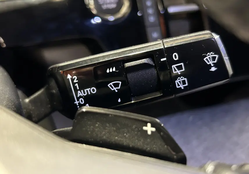 Gros plan sur la commande des essuie-glaces du Peugeot 5008 III Hybrid 145, avec levier noir et symboles blancs.