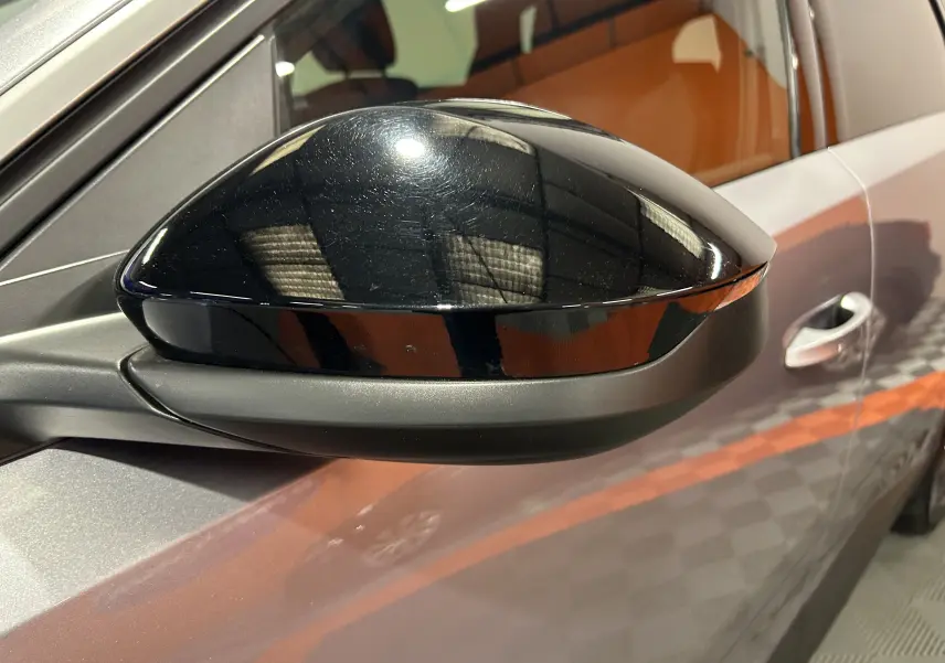 Gros plan sur le rétroviseur noir brillant côté gauche d’un Peugeot 5008 gris Artense, avec porte et vitre partiellement visibles.