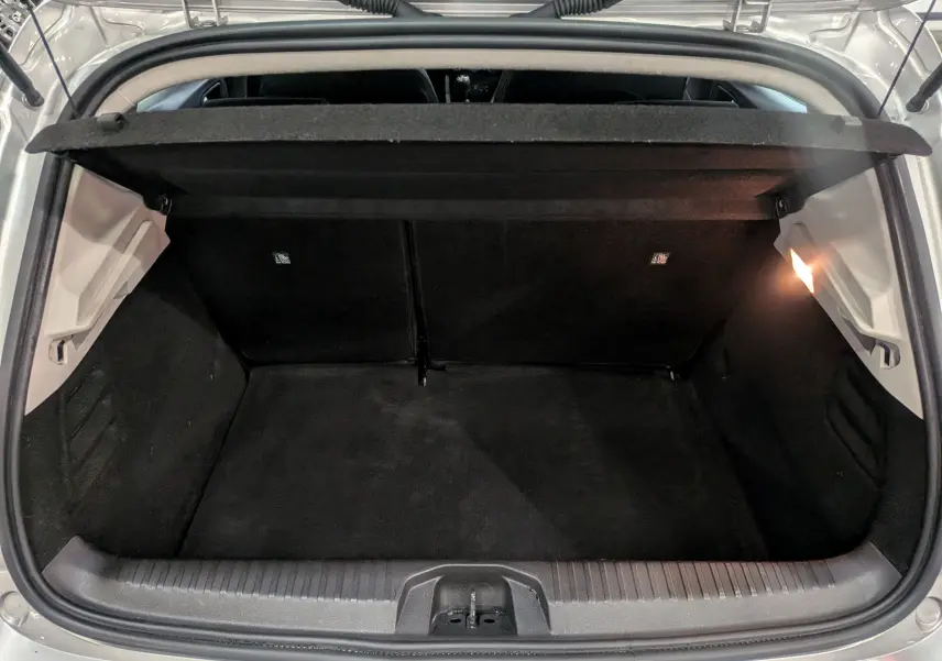 Vue intérieure du coffre ouvert d'une Renault Clio V gris platine, montrant l'espace de rangement et l'éclairage latéral.