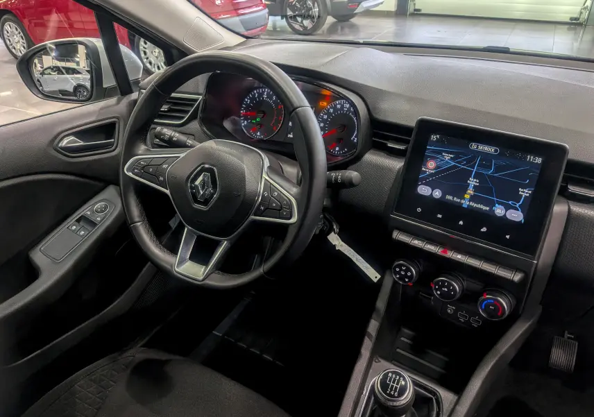 Vue intérieure côté conducteur de la Renault Clio V TCe 90 Gris Platine, tableau de bord avec écran tactile et levier de vitesse manuel.