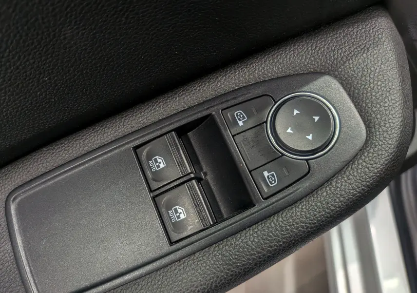 Gros plan sur les commandes de lève-vitres et réglage des rétroviseurs côté conducteur d’une Renault Clio V gris platine.