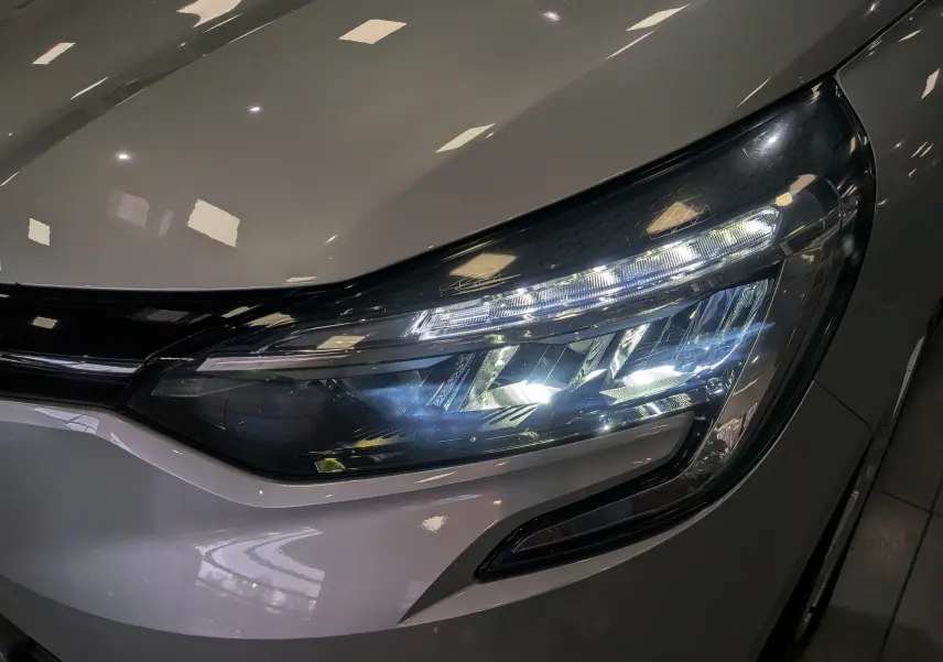 Gros plan sur le phare avant droit allumé d'une Renault Clio V gris platine, soulignant ses lignes modernes et LED.