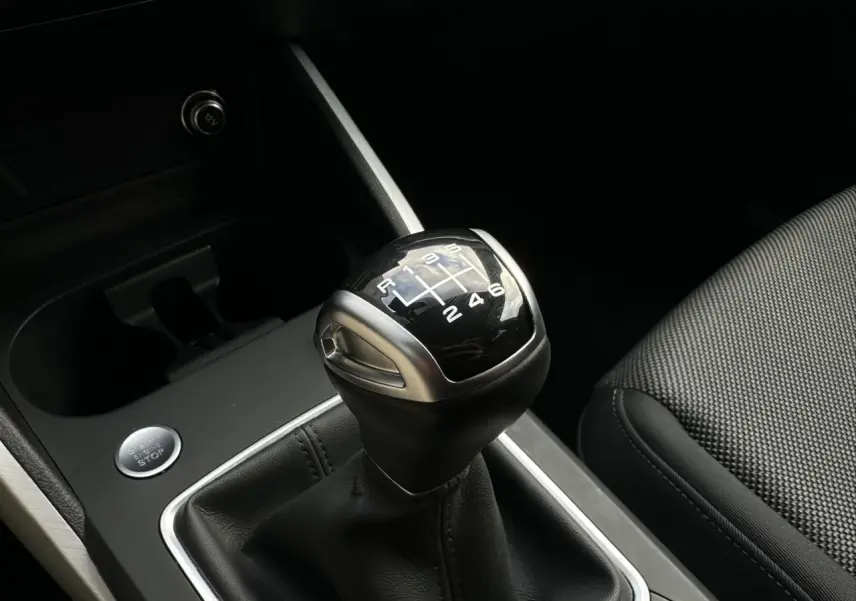 Gros plan sur le levier de vitesses manuel noir et argenté de l'Audi Q2 30 TFSI 110 S-Line 2024, intérieur sombre.