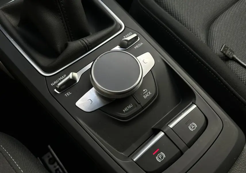 Vue rapprochée de la console centrale noire de l'Audi Q2 30 TFSI S-Line 2024 avec commandes multimédia et frein électrique.