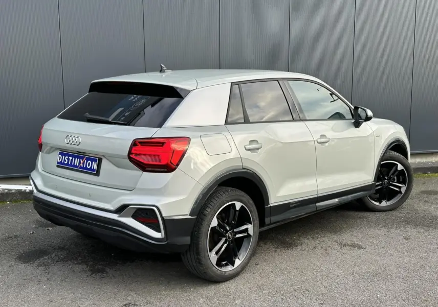 Audi Q2 30 TFSI S-Line argent rosé, vue 3/4 arrière droit, jantes noires brillantes et vitres surteintées.