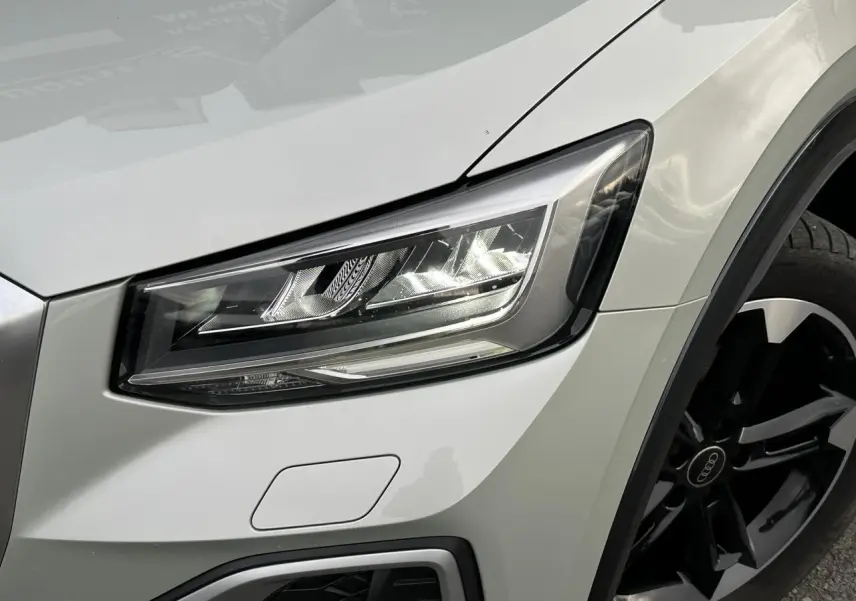 Gros plan sur le phare avant droit et la jante noire polie d’un Audi Q2 30 TFSI S-Line argent rosé.