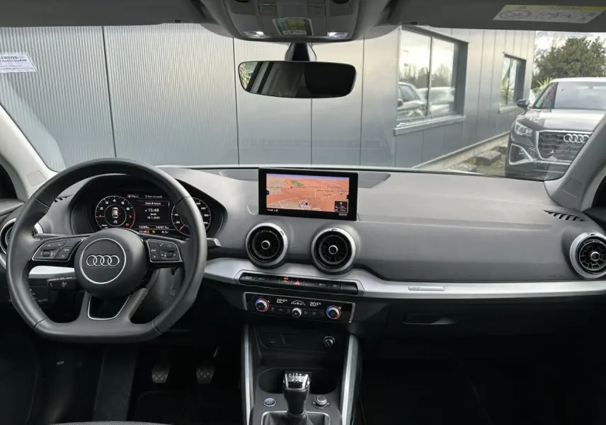 Vue intérieure de l'Audi Q2 30 TFSI S-Line 2024, tableau de bord avec écran central et volant multifonction cuir.