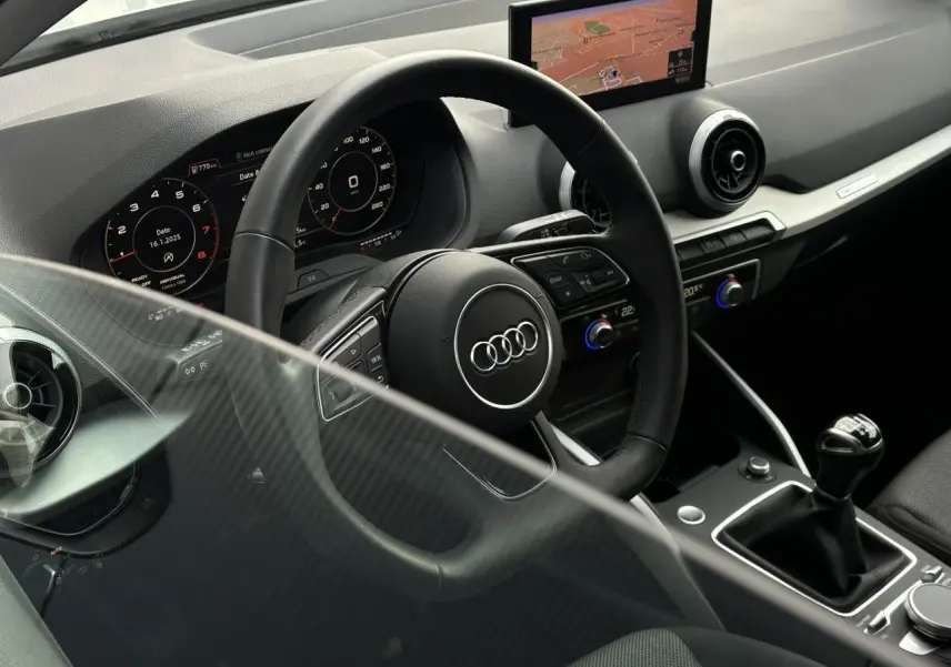 Vue intérieure côté conducteur de l'Audi Q2 30 TFSI S-Line 2024, volant cuir, écran navigation et levier de vitesses manuel.