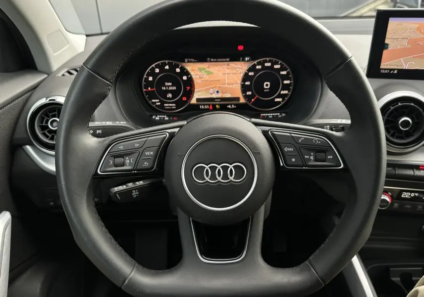 Vue rapprochée du volant cuir noir multifonction et du tableau de bord numérique de l'Audi Q2 argent rosé 2024.