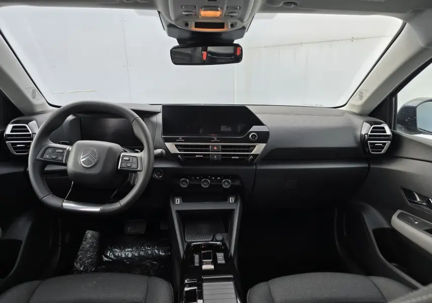 Vue frontale de l'intérieur noir du Citroën C4 III hybride 2025 avec tableau de bord épuré et écran tactile central.