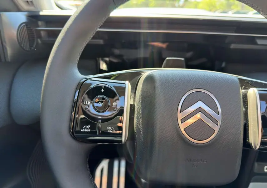 Gros plan sur le volant cuir multifonctions noir avec logo Citroën, tableau de bord numérique en arrière-plan.