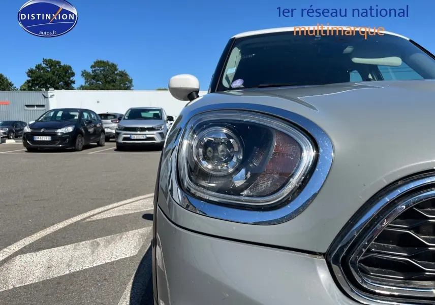 Gros plan sur le phare avant gauche et la calandre chromée d'une MINI Countryman Moonwalk Grey, toit et rétroviseurs blancs.