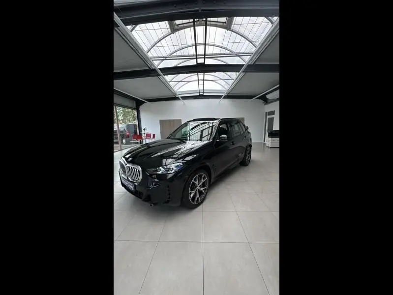 BMW X5 xDrive50e noir en 3/4 avant droit dans un showroom lumineux avec jantes alliage et calandre chromée.