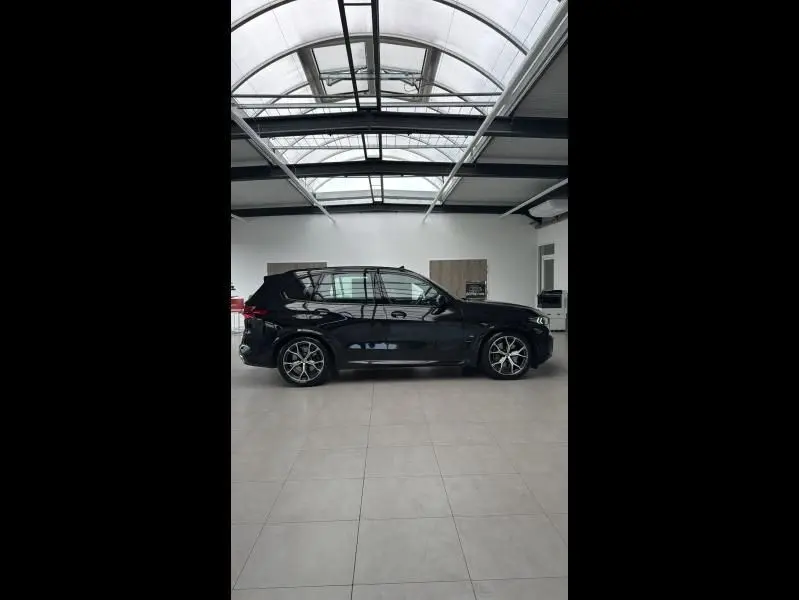 Profil côté gauche d’un BMW X5 xDrive50e noir brillant, avec jantes alliage et toit ouvrant panoramique en intérieur showroom.