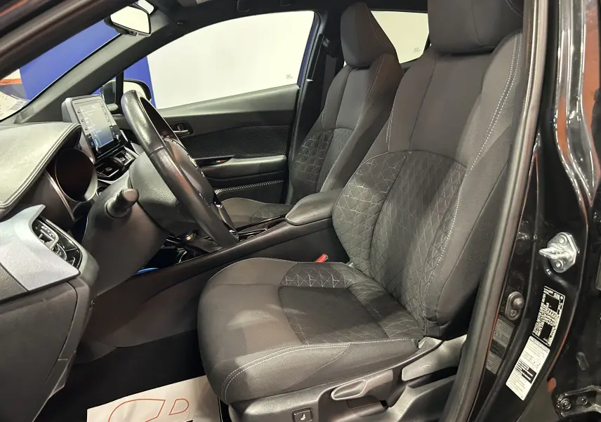 Vue intérieure côté conducteur du Toyota C-HR Hybride noir métal 2021, sièges tissu avec motifs géométriques et tableau de bord moderne.